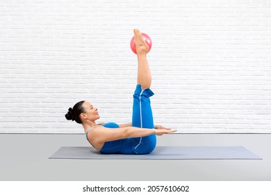 Pilates recovery. Attractive adult woman lying on back, lift up straight legs with small ball between feet, the hundred drill in fitness studio indoor.