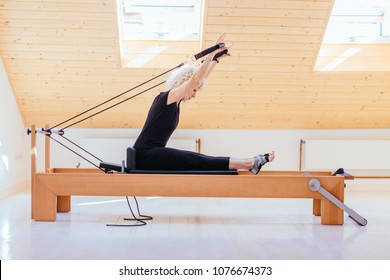 Pilates reformer eldery blond curly woman gym fitness teacher workout back and hands exercise on pilates reformer device - pilates, fitness, sport, training and people concept.