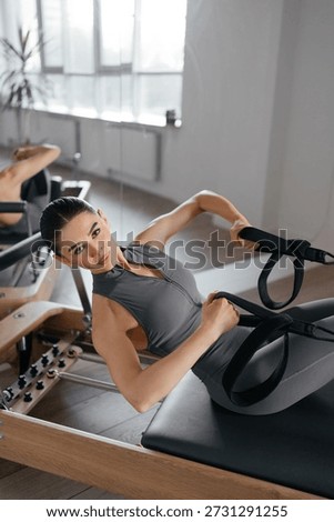Pilates reformer training machine in active use showing springs and modern mechanical details. Female athlete controls movement with precision highlighting functionality design and effectiveness 