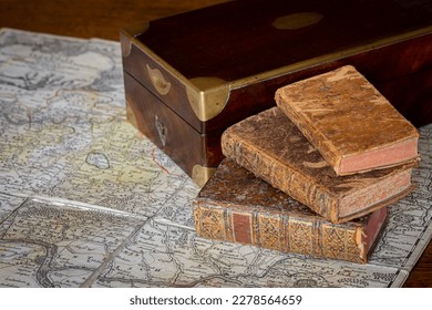 Pile of antique books with a leather cover and golden ornaments, close to a wooden box on an ancient topographic map - Powered by Shutterstock