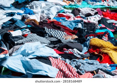 pile of assorted second hand clothes and shoes laid out on the ground, outdoor flea market scene, colorful clothing items in disarray, concept of sustainable fashion, recycling, vintage shopping