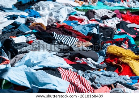pile of assorted second hand clothes and shoes laid out on the ground, outdoor flea market scene, colorful clothing items in disarray, concept of sustainable fashion, recycling, vintage shopping