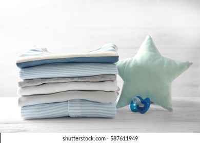 Pile Of Baby Clothes And Pacifier On Wooden Table