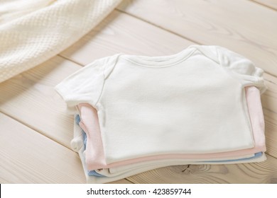 Pile of baby shirts on wooden desktop. Mock up