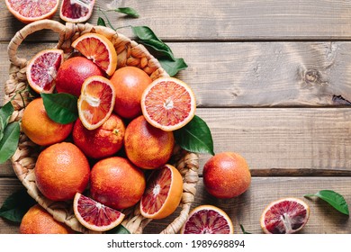Pile of blood oranges in a basket on a wooden table background. Flat lay, top view, copy space.