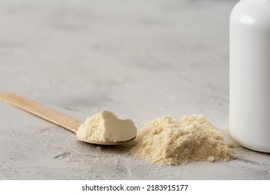 Pile of bovine colostrum powder with wooden spoon and white container on white background. Colostrum benefits for immune system and gut health concept