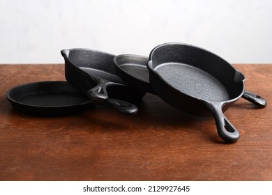 pile of cast iron skillets on old wood table - Shutterstock ID 2129927645