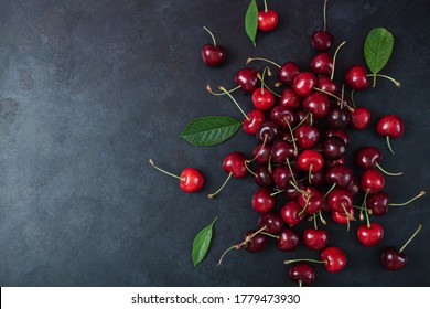 Pile of cherry with leaf and water drops on black stone table. Ripe ripe cherries. Sweet red cherries. Top view. Rustic style. Fruit Background