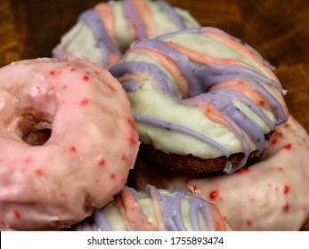 Pile Of Cherry And Mixed Berry Donut / Doughnuts On A Wooden Cutting Board With A Pink Cherry Glaze And A White Glaze With Blue And Pink Drizzle.  Delicious Baked Goods.