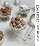 A pile of chocolate truffles dusted with cocoa powder on a glass pedestal. Other bowls of truffles and powdered sugar are visible in the background.