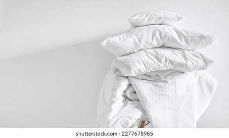 pile of clean blanket, linen bedding, cotton sheets, cushions and duvet with natural material on chair after laundry on white wall background with copy space - Shutterstock ID 2277678985