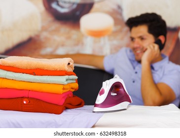 A Pile Of Clothes Next To The Iron With Gorgeous Man Smiling Behind While He Is Using A Celphone