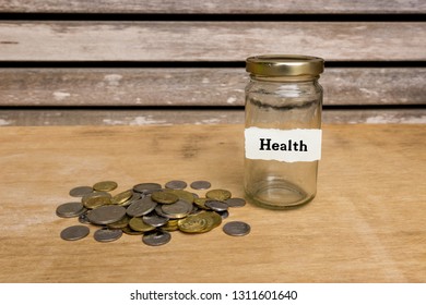 Pile of coins beside am empty jar attached with label written Health on wooden background. Saving for health concept.