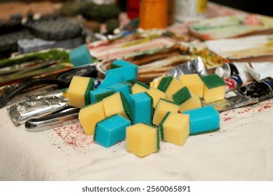 Pile of colorful cleaning sponges on a table amidst artistic supplies. - Powered by Shutterstock