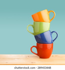 Pile of colorful cups on wooden table on blue background