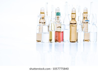 Pile of colorful transparent glass ampoules with liquid medicine isolated on abstract white background. Healthcare, medical, pharmaceutical and beauty concept. Closeup with soft selective focus Toned
