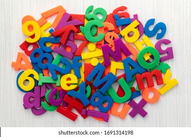 A Pile Of Coloured Magnetic Letters And Numbers Over A Wooden Table