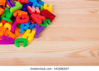 A Pile Of Coloured Magnetic Letters Over A School Wooden Table