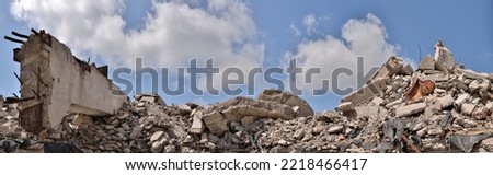 A pile of concrete gray debris of a destroyed building with a huge beam in the foreground against a blue sky with clouds. Panorama.