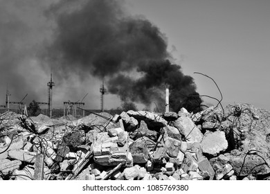 A Pile Of Concrete Rubble With Protruding Rebar On The Background Of Thick Black Smoke In The Sky. Background. The Concept Of The Consequences Of Human Activities. Black And White Image.