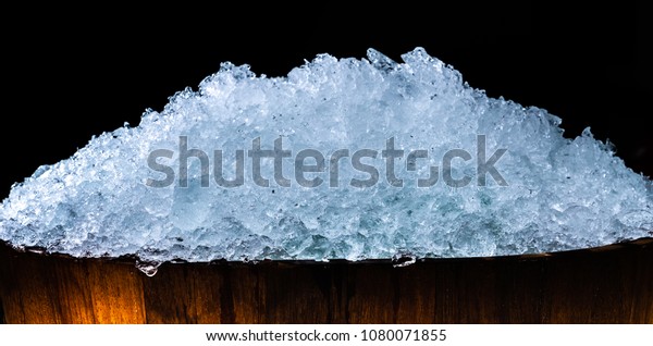 Pile\
of crushed ice cubes in wood bucket on dark background with copy\
space. Crushed ice cubes foreground for beverages, beer, whisky,\
fruit juice, milk, fresh food or fresh\
vegetables.