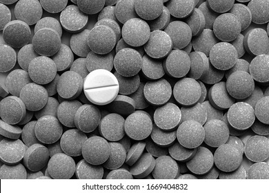 Pile of dark pills around a white one, low key monochrome. Medication, self-treatment or placebo concept: one tablet is different from the lot of others