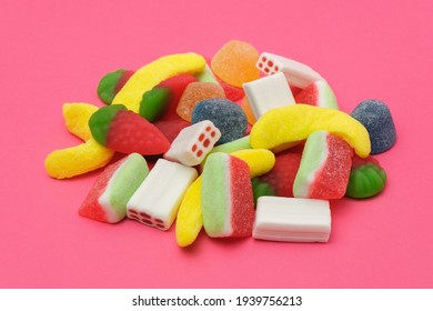 Pile of delicious colorful, tasty candies of different shapes on a pink background.