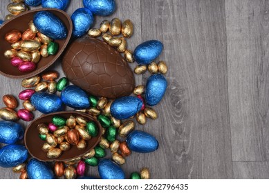 Pile of different sizes of colourful foil wrapped chocolate easter eggs in pink, blue, gold and green. Large halves of a brown milk chocolate egg have mini eggs inside, on a grey wooden background. - Powered by Shutterstock