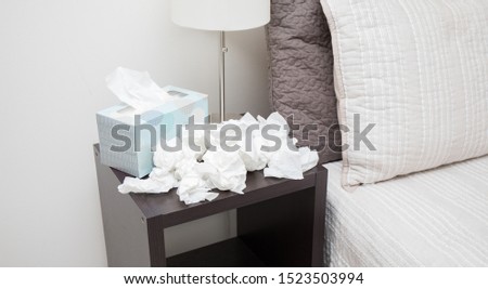 A pile of dirty, used, and crumpled up tissues on a nightstand.
