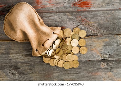 Pile of dollar coins spilling out of a drawstring pouch onto a rustic old weathered wooden table, view from above with copy space