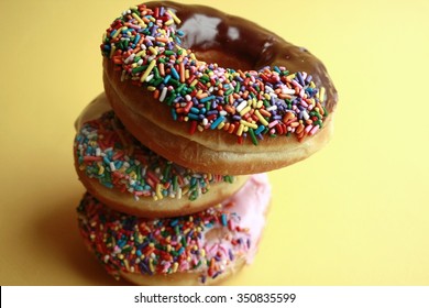 Pile of Donuts with sprinkles with a yellow back ground/Donut Pile/Donuts with sprinkles