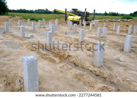 A pile driving mechanism operating on a construction site.Concrete piles or pillars are dug into the ground. The construction of a monolithic building or bridge has begun.Development of the district