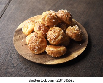 pile of French Chouquettes coated with white pearl sugar on wooden plate and background