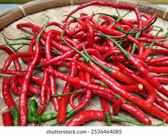 a pile of fresh red chili peppers with bright red color and green stalks still attached are placed on a woven bamboo tray - Powered by Shutterstock