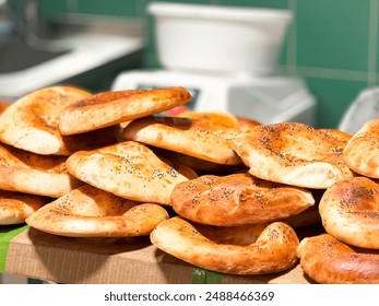 Pile of freshly baked traditional round bread with golden brown crust and sprinkled with black sesame seeds, stacked on cardboard surface in kitchen setting with tiles and scale in background. - Powered by Shutterstock