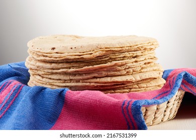 Pila de tortillas recién hechas sobre un paño o servilleta rosado y azul mexicano en una canasta.