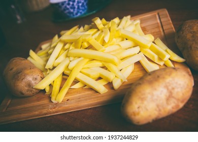 A pile of fries, potatoes cut into bars on a wooden board on a table, can be fried in a deep fryer or airfryer 
