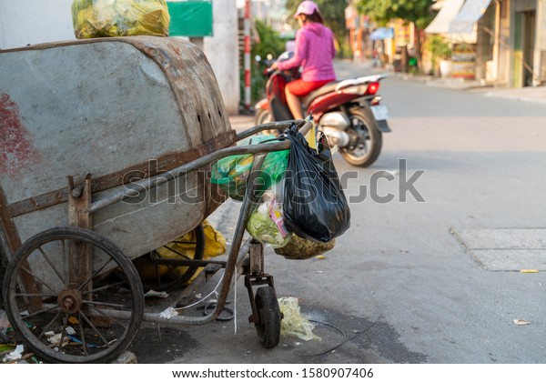 Pile of garbage bags and\
messy trash on street sidewalk with traffic on background in Hanoi,\
Vietnam