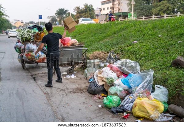 Pile of garbage bags and messy trash on street\
sidewalk with traffic on background in Hanoi, Vietnam. A man\
dumping rubbish into\
dustbin