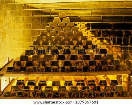 A pile of gold bars in front of a golden wall; golden ingots