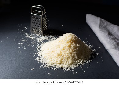 A Pile Of Ground Parmesan Cheese Next To A Mini Grater And A Napkin. Dark Style.