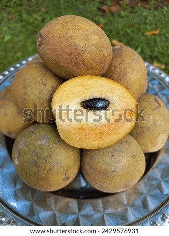 Pile of honey type sapodilla fruit on a tray. This fruit is brownish when ripe and has a soft, slightly wrinkled texture with black seeds.