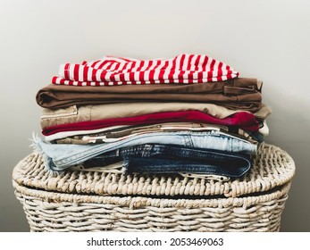 A pile of ironed colorful female clothes on a white wicker basket ready to be organised in wardrobe. Horizontal. Selective focus on basket
