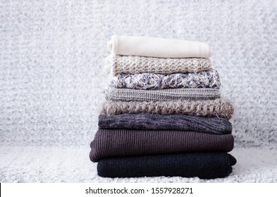 Pile knitted woolen sweaters  Monochrome gradient shades grey white black colors clothes and different knitting patterns folded in stack  Warm cozy winter autumn knitwear concept  Copy space 