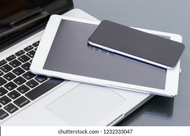 Pile Of Laptop Computer And Digital Tablet Electronic Devices With Blank Black Screen On Table In Office