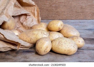 A Pile Of Maris Piper An English Favourite Potatoes Spilling Out Of A Brown Paper Sack Onto An Old Wooden Table.