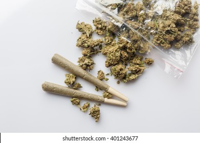 Pile of medical cannabis dried buds scattered from nylon package and two marijuana joints on white background directly from above