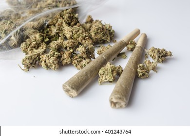 Pile Of Medical Cannabis Dried Buds Scattered From Nylon Package And Two Marijuana Joints On White Background From Side