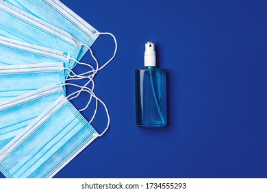 Pile Of Medical Face Masks With Hand Sanitizer On Blue Background Close Up