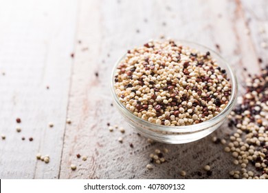 Pile of mixed raw quinoa, South American grain, in glass bowls on white rustic wooden background. Healthy and gluten free food. Copy space.